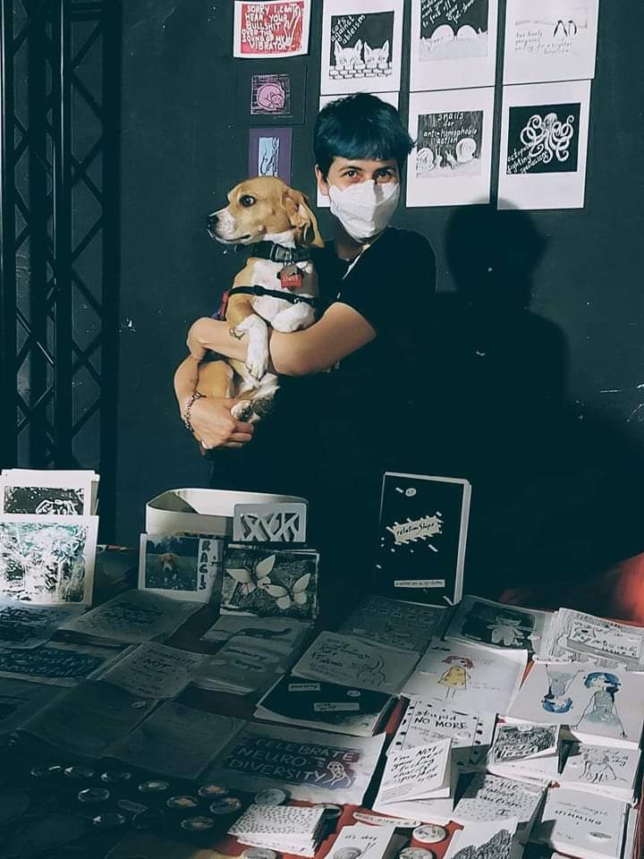 Lex with their dog Ragis surrounded by their art