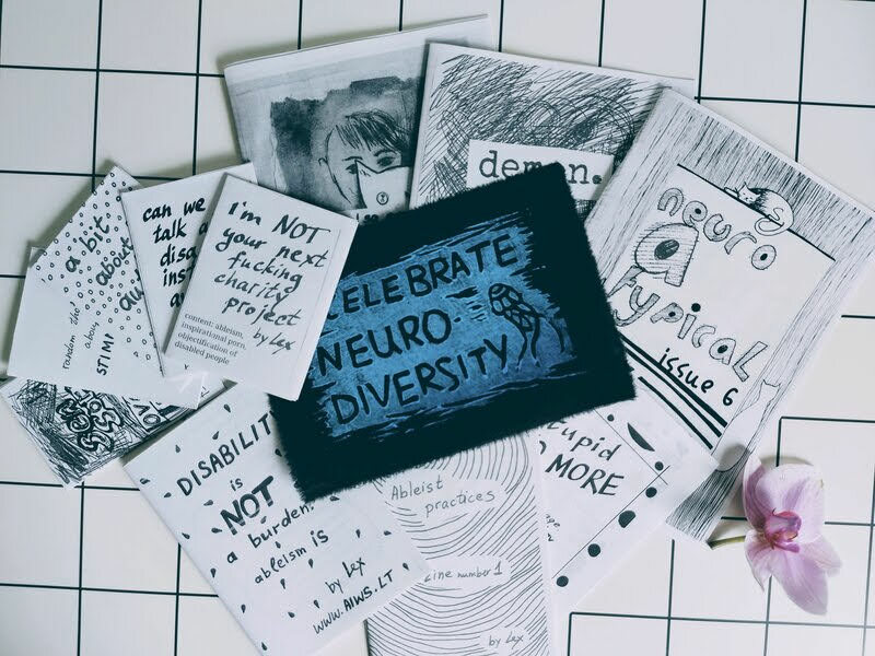multiple zines and a blue patch with a words "neurodiversity is beautiful"
